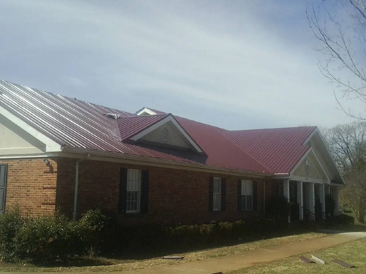 Red metal roof with gabled entries on a long brick building, from a Hail Damage Roof Repair job in Chenango Forks