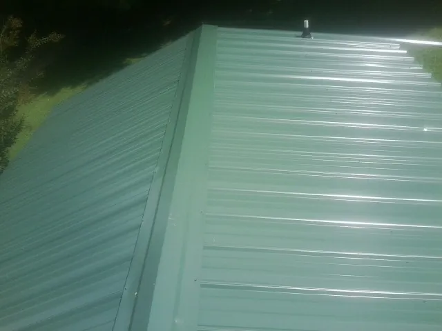 New green metal panels meeting at the ridge of a roof — Flat Roof Repair work by our crew in Chenango Forks