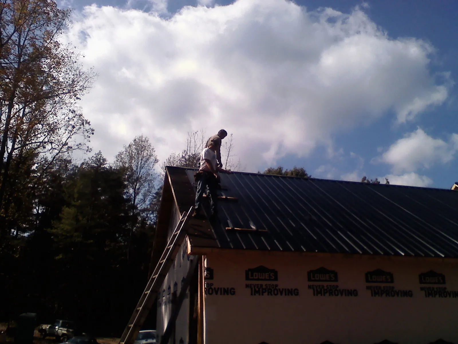 Roofer fastening dark metal panels high against a cloudy sky, from a Roof Inspection job in Chenango Forks