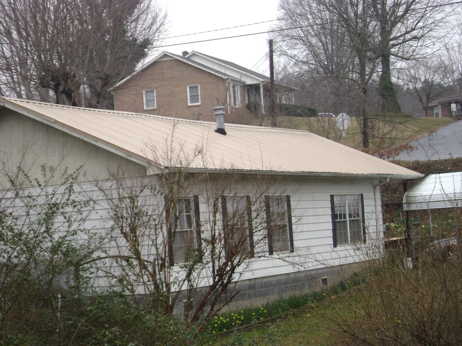Tan metal roof on a white sided house set into a hillside — Commercial Roofing by Roofing Brothers in Chenango Forks
